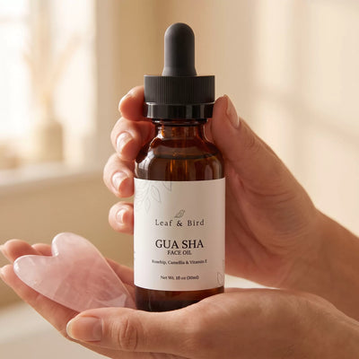 Gua Sha Face Oil amber dropper bottle held in hand next to a rose quartz gua sha