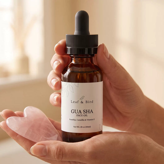 Gua Sha Face Oil amber dropper bottle held in hand next to a rose quartz gua sha