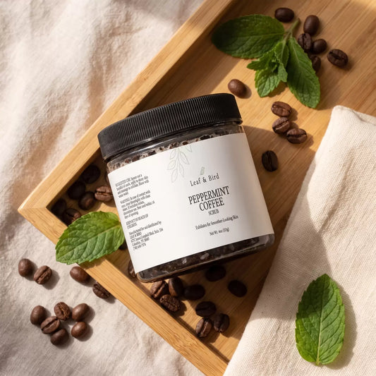 Leaf & Bird Peppermint Coffee Scrub jar on a wood tray with coffee beans and mint